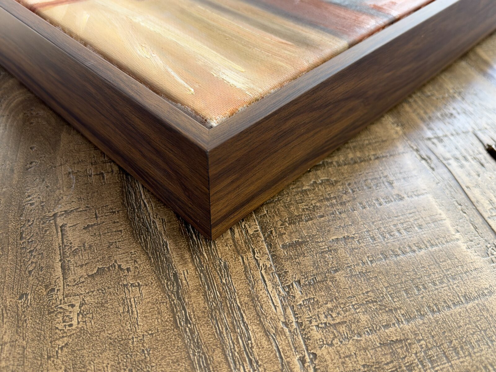 Close-up of a walnut frame corner meeting the edge of an oil painting.